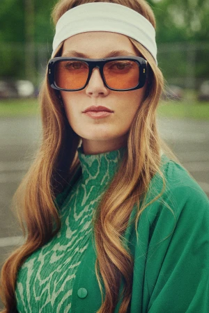 Portrait of a woman wearing orange-tinted sunglasses, a white headband, and a green patterned top styled by Kinsey Ranee.