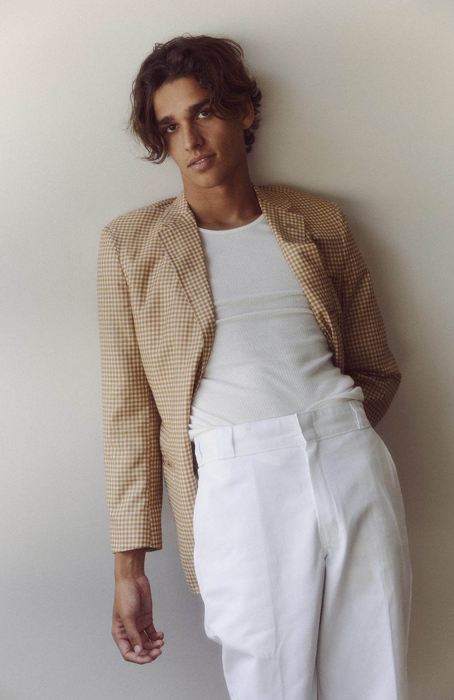 Young adult male posing in a studio, wearing a blazer, t-shirt, and pants, with a soft light highlighting his features and outfit details.