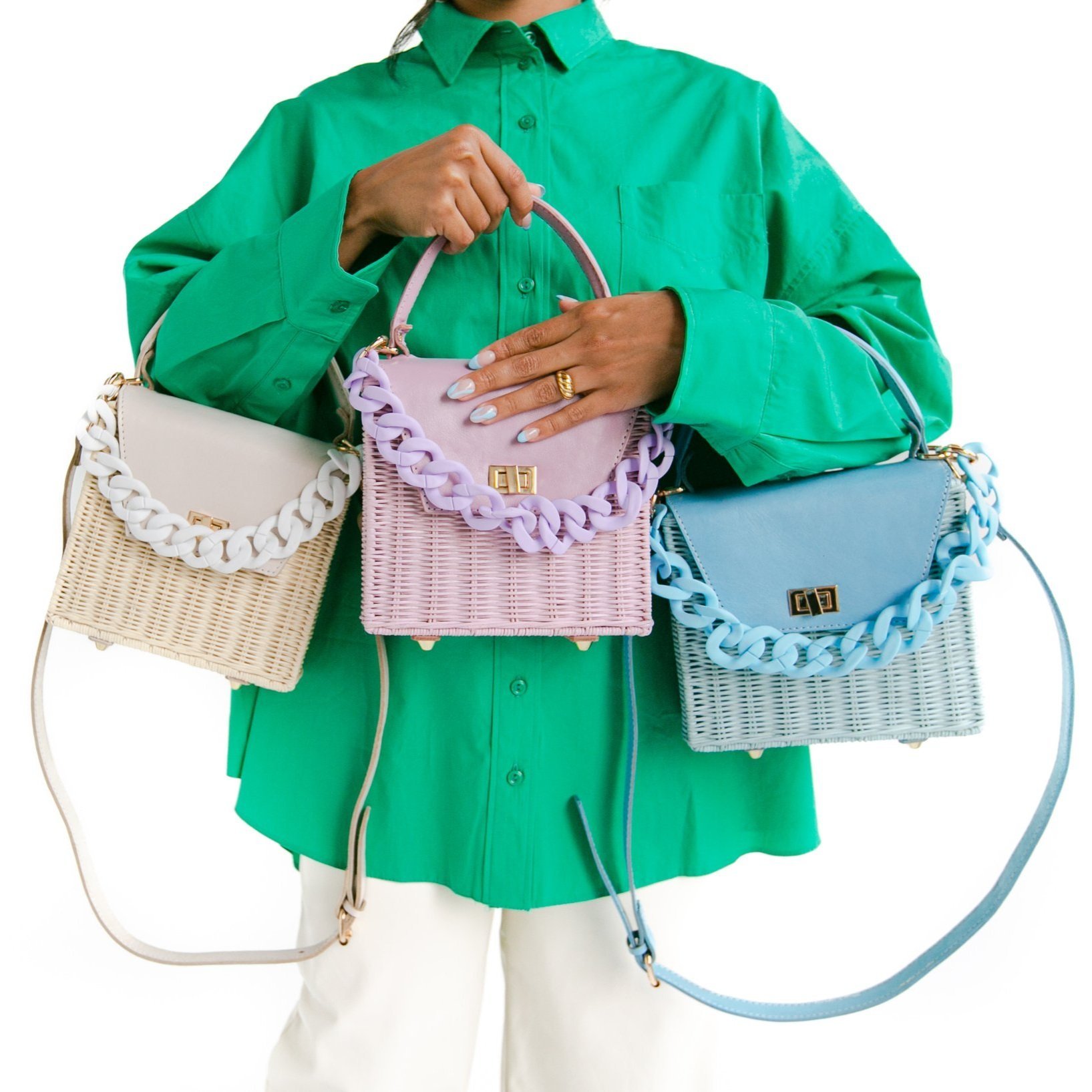 Woman in green shirt presenting three pastel-colored woven handbags with chain accents, against a white background in a studio setting.
