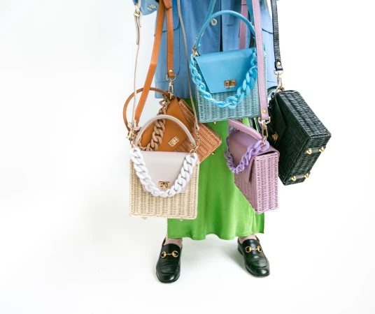 Person holding multiple colorful woven wicker handbags with chunky chain straps against a white background