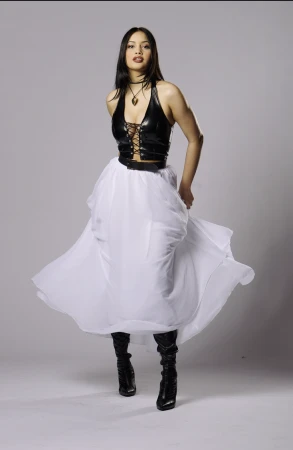Model wearing a black lace-up halter top and a long white skirt against a plain grey backdrop