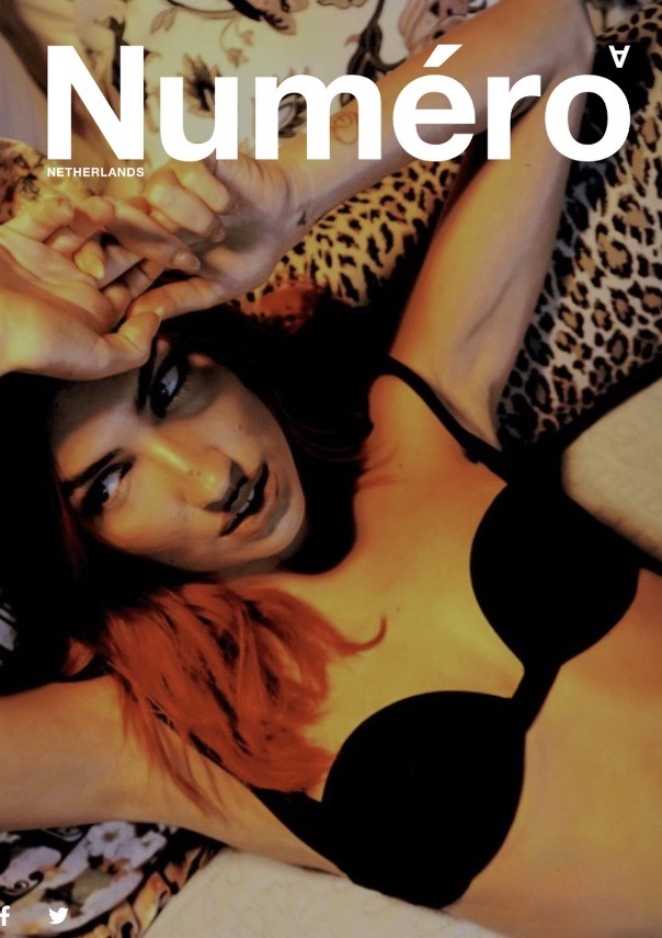 Magazine cover featuring a woman with red-tipped hair wearing a black bra, posing with hands up against a floral background.