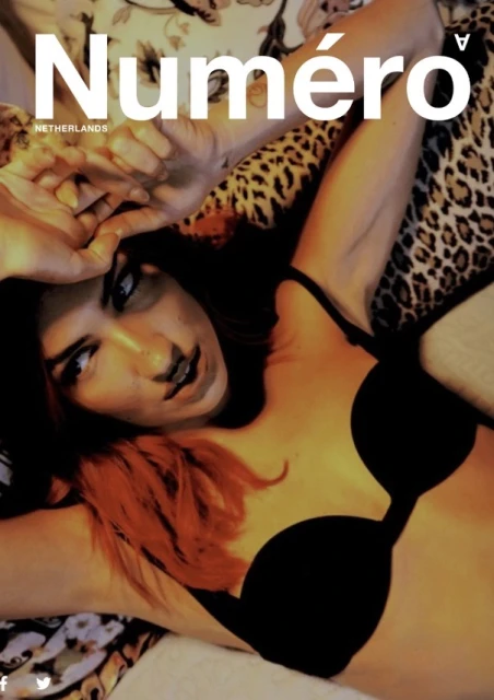 Magazine cover featuring a woman with red-tipped hair wearing a black bra, posing with hands up against a floral background.