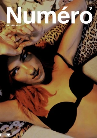 Magazine cover featuring a woman with red-tipped hair wearing a black bra, posing with hands up against a floral background.