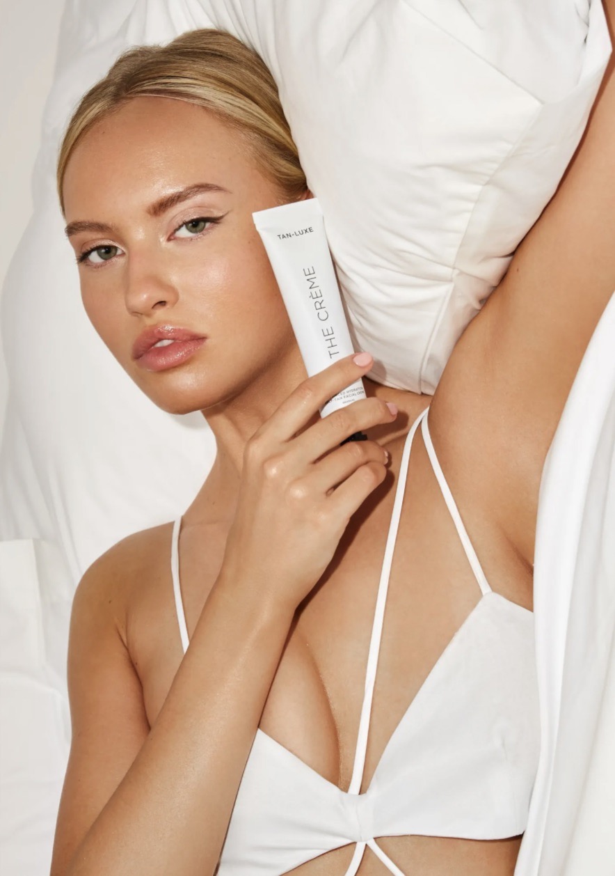 Adult female posing with beauty product against a white background wearing white top, natural makeup, and hair. Beauty shot.
