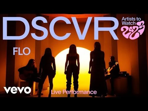 Music video performance by FLO, a female music group, featuring silhouettes against a vibrant orange backdrop and band members playing instruments.