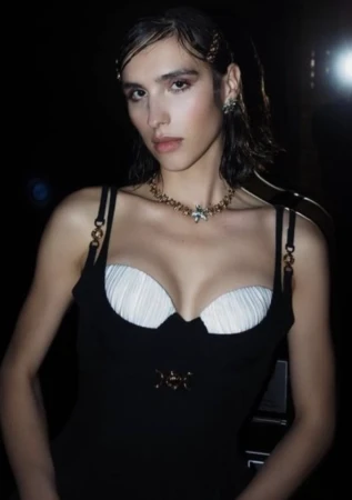 A woman wearing a black dress with white bustier cups and a gold statement necklace, styled by Kirsty Stewart.