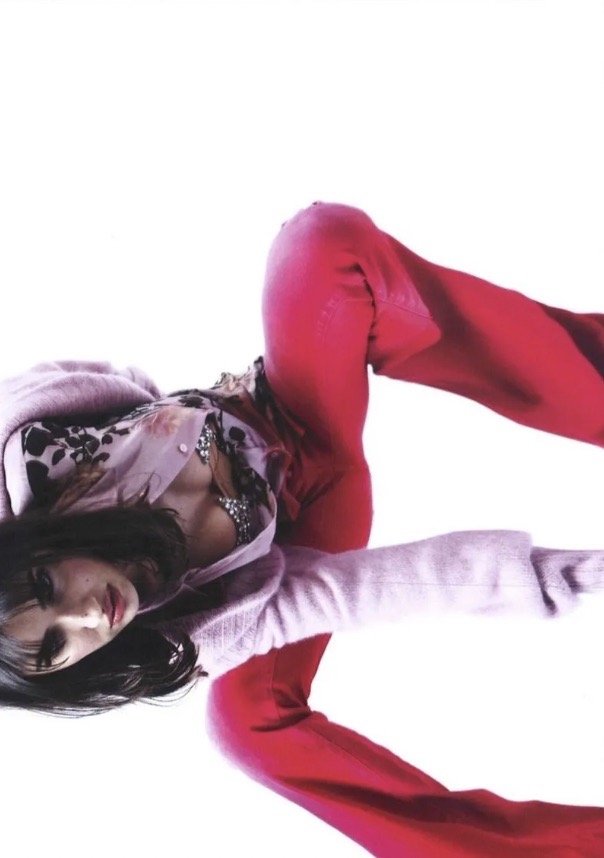 A slender adult female lies reclined in a photo studio with white backdrop, wearing pink slacks and a sweater. The subject is well lit.