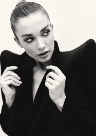 Monochrome portrait of a woman with dark hair in a bun wearing a structured black jacket against a plain background