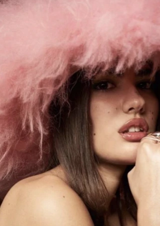 Close-up portrait of a woman wearing a large fluffy pink hat and silver rings styled by Kirsty Stewart.