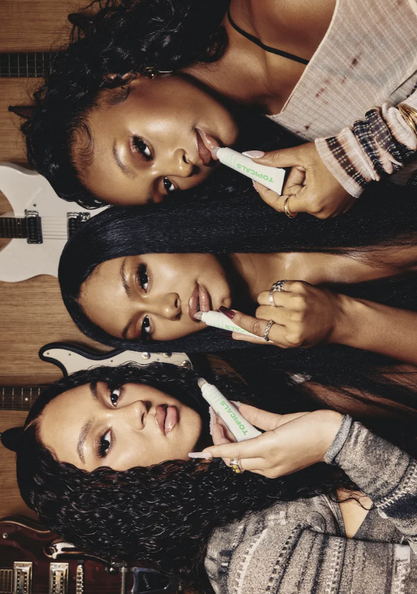 Three women pose together with beauty product in hand; one woman has curly hair, one has straight hair, and one has a bun.