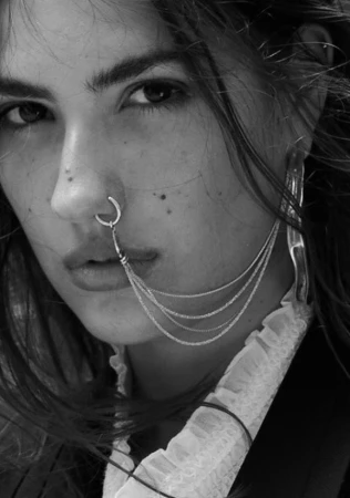 Close-up monochrome portrait of a woman wearing facial chain jewellery and a ruffled high collar top styled by Kirsty Stewart.