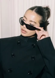 Close-up portrait of a woman wearing dark sunglasses and a black double-breasted jacket styled by Kirsty Stewart.