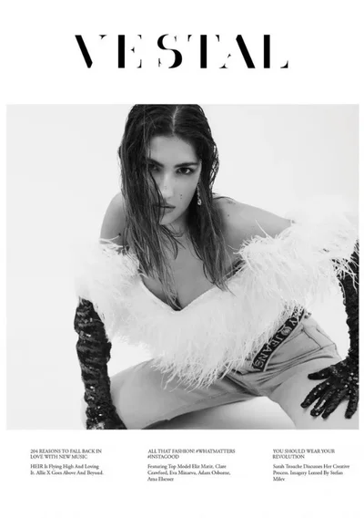 Model in white feather top and black sequined gloves kneeling against a white backdrop for a fashion magazine cover.