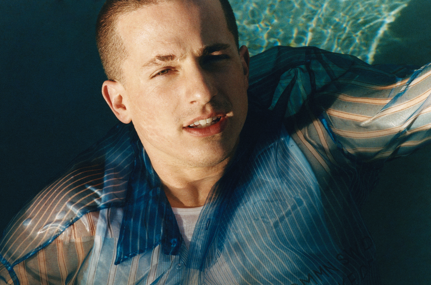 Man in blue striped shirt lying in water with ripples, creating a serene, slightly backlit outdoor portrait.