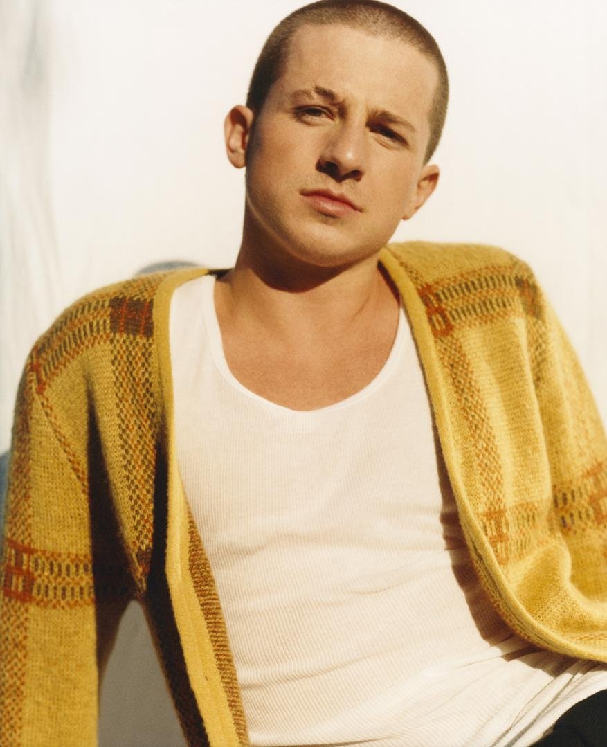Portrait of adult male wearing a tank top and cardigan sweater, gazing at the camera in a brightly lit indoor setting.