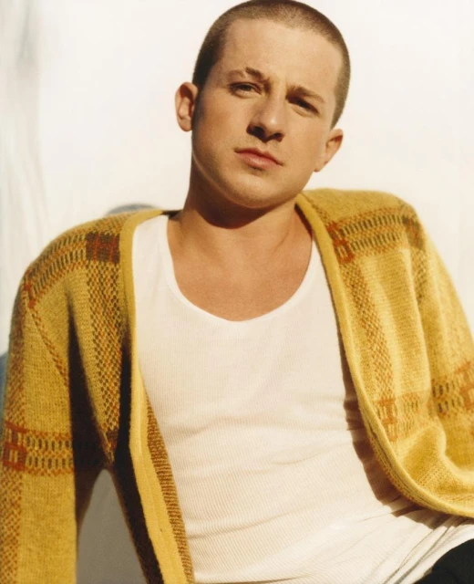 Portrait of adult male wearing a tank top and cardigan sweater, gazing at the camera in a brightly lit indoor setting.