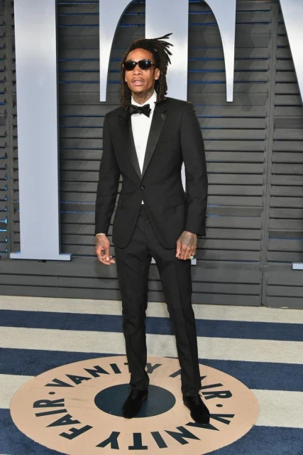 Wiz Khalifa in a black tuxedo and sunglasses poses on a striped circle for the Vanity Fair Oscar party red carpet.