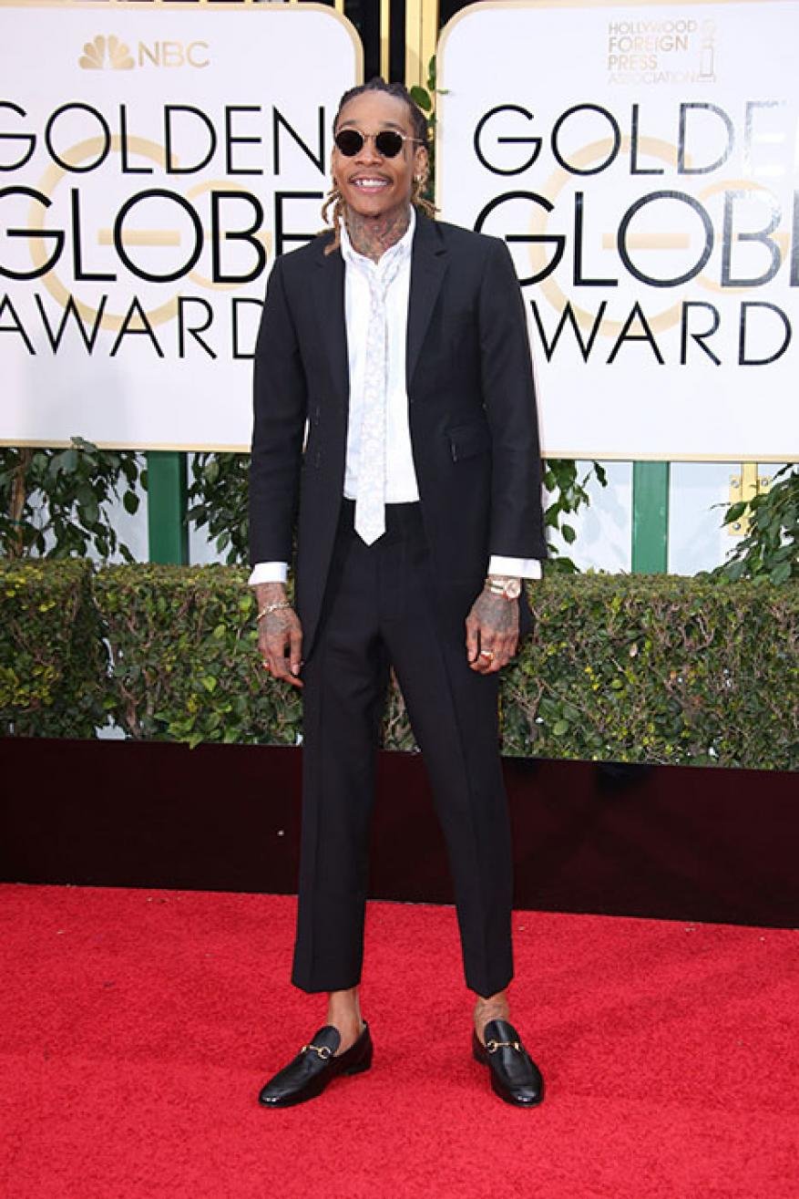 A man in a black suit poses on a red carpet at an awards show in front of a Golden Globe Awards backdrop for a formal celebrity event.