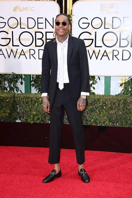 A man in a black suit poses on a red carpet at an awards show in front of a Golden Globe Awards backdrop for a formal celebrity event.