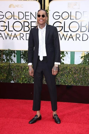 A man in a black suit poses on a red carpet at an awards show in front of a Golden Globe Awards backdrop for a formal celebrity event.