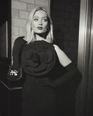 Black and white editorial portrait of a woman in a dark dress with a large floral appliqué and opera gloves, styled by Lauren Matos.