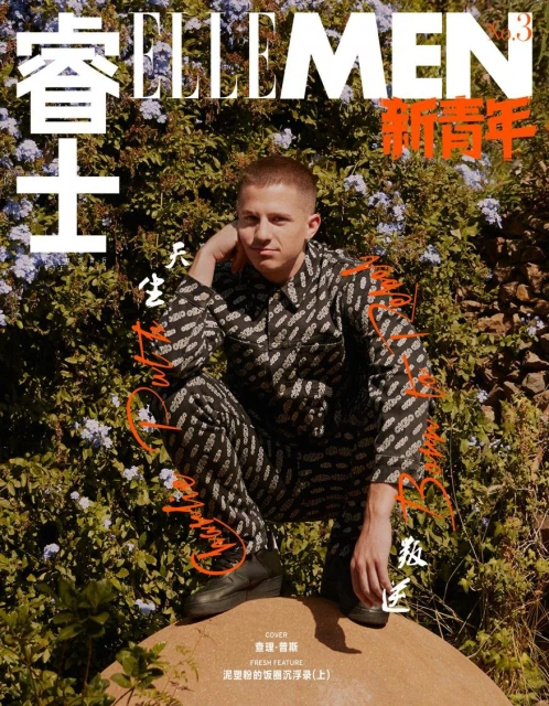 Elle Men magazine cover featuring a male model in a patterned jumpsuit crouching outdoors with a floral background in warm lighting.