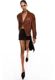 Model wearing a brown leather jacket and black skirt walking against a bright white background