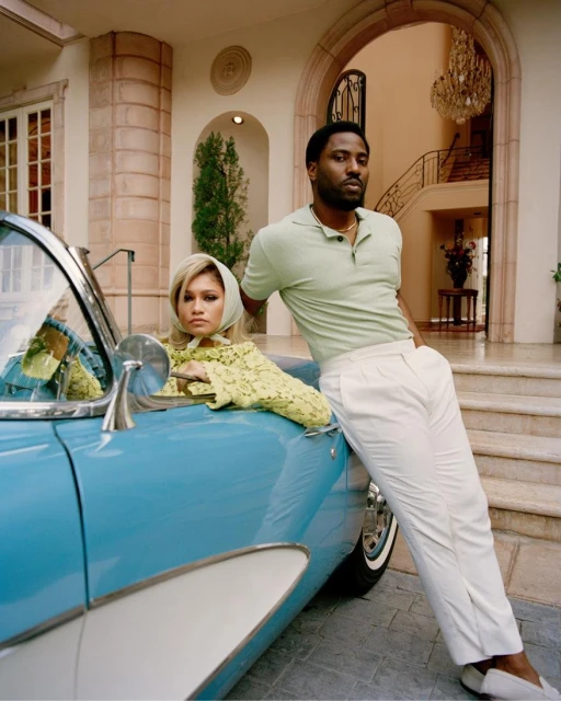 Fashion shot of a couple with a vintage car outside a mansion: Zendaya in the driver's seat and John David Washington leaning against the door.