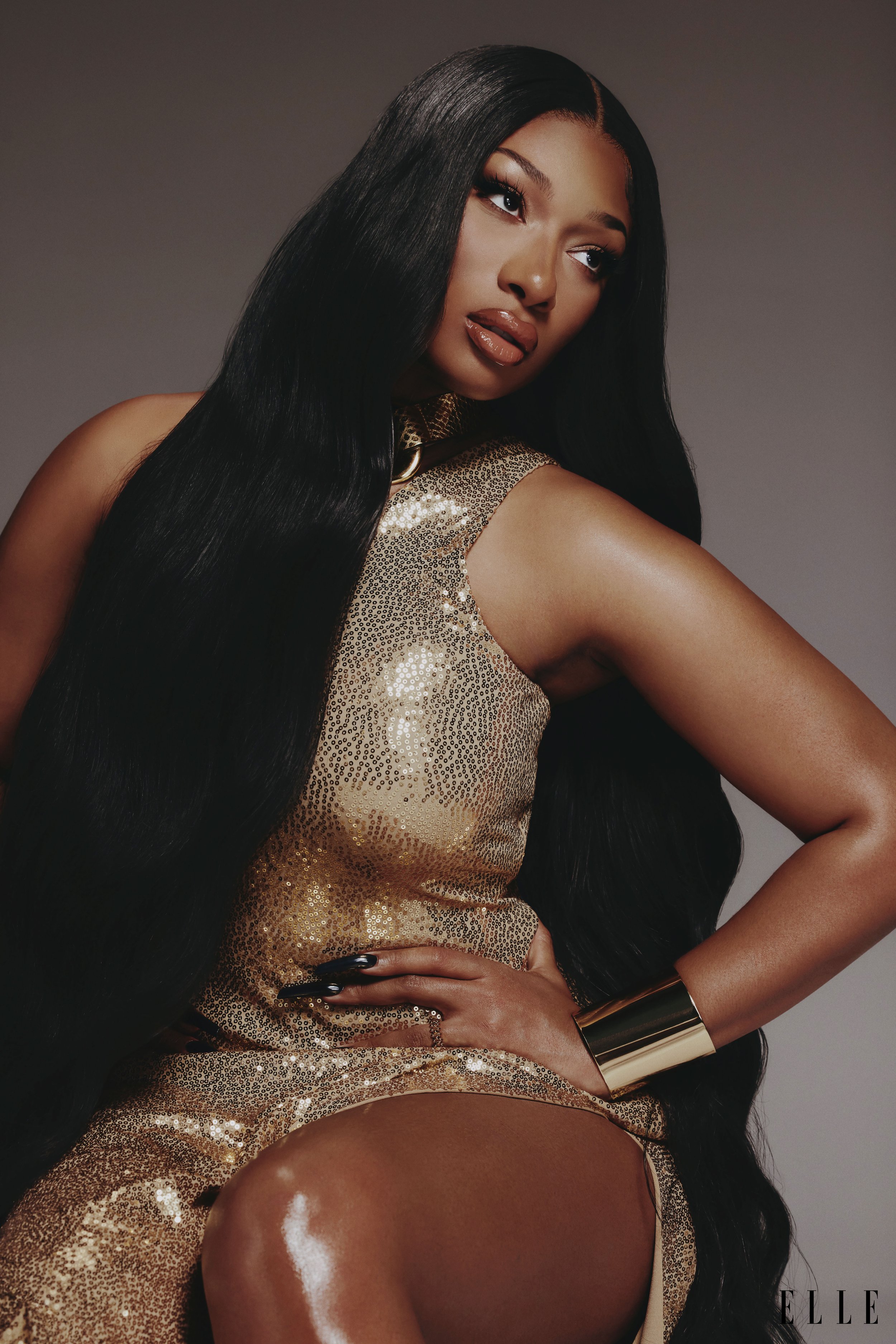 Portrait of a Black woman with long black hair and a golden sequined dress. She poses in a studio setting with elegant lighting.