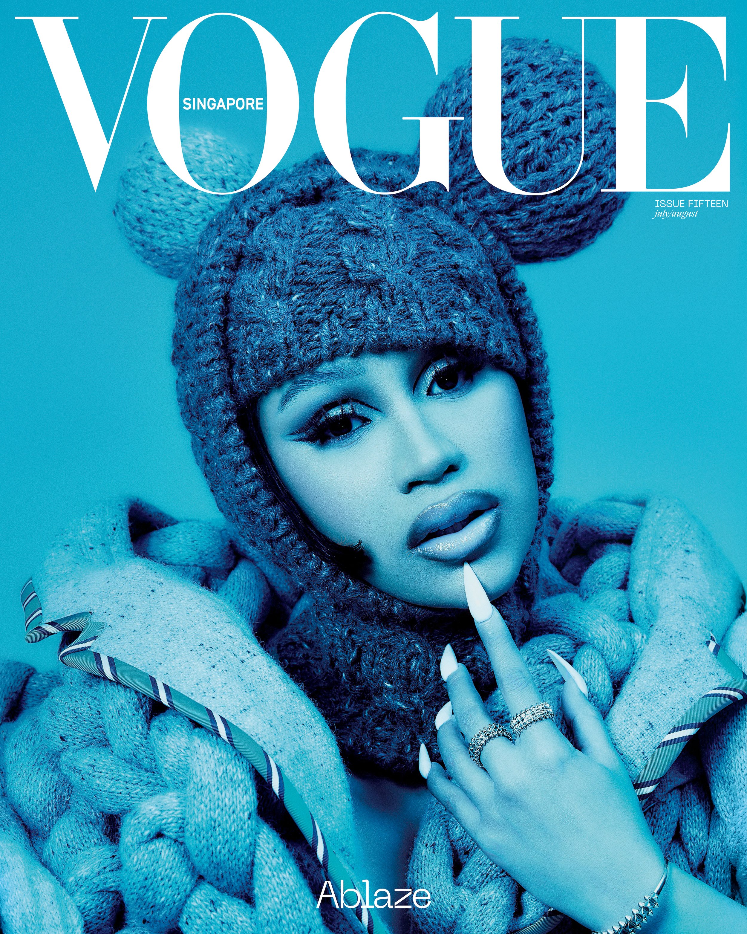 Vogue Singapore cover featuring a person with dramatic eye makeup, wearing a knitted hat with ear-like adornments, against a blue background.