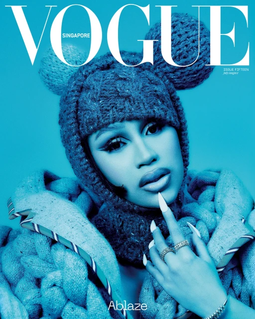 Vogue Singapore cover featuring a person with dramatic eye makeup, wearing a knitted hat with ear-like adornments, against a blue background.
