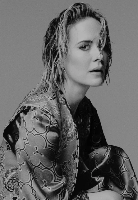 Black and white portrait of a blonde adult woman with short wet hair, wearing a patterned robe, looking at the camera. 