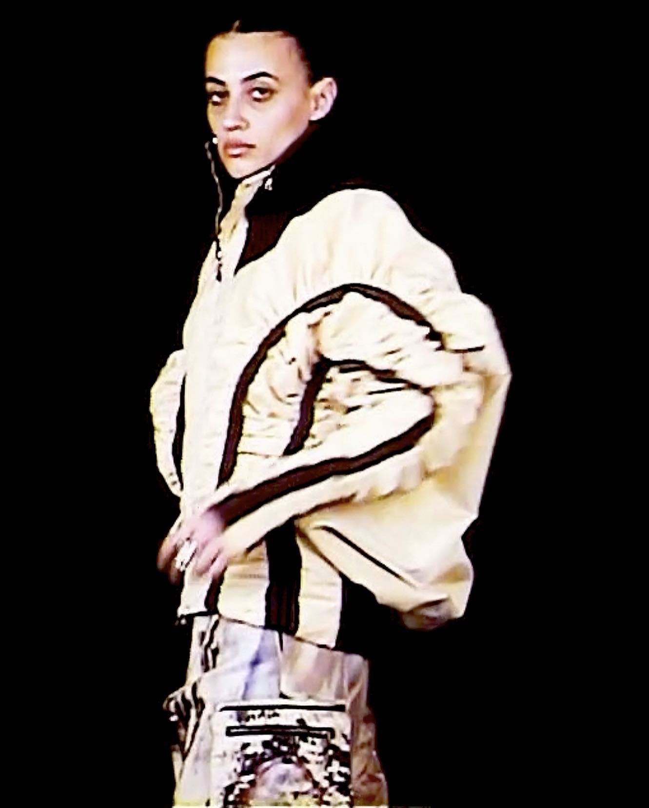Model wearing a structured cream jacket with dark trim styled by Lee Trigg against a black background.