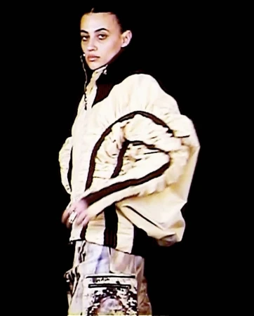 Model wearing a structured cream jacket with dark trim styled by Lee Trigg against a black background.