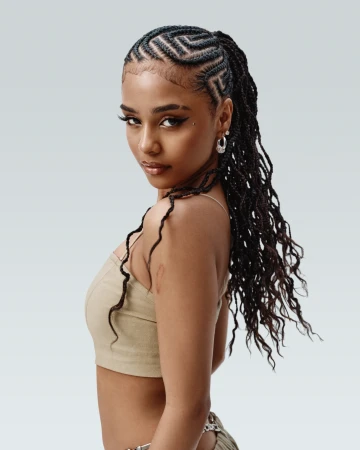 Portrait of a young woman with braided hair, wearing a neutral-toned crop top, posing in front of a light grey backdrop in a studio setting.