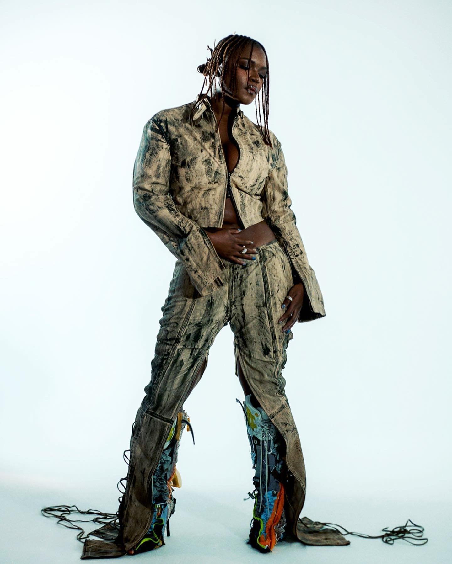 Woman in distressed printed matching jacket and pants standing against a plain white studio backdrop.
