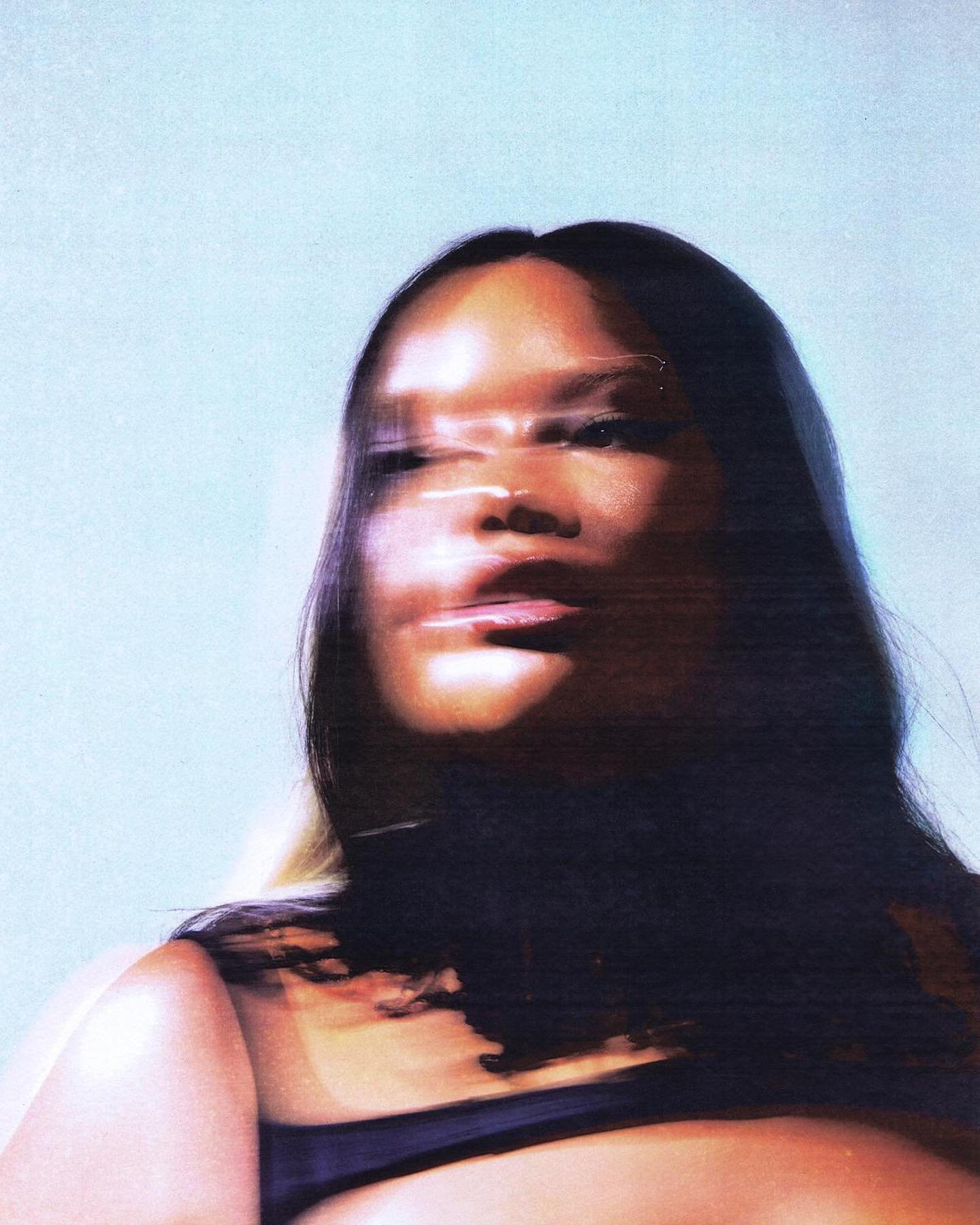 Portrait of an African-American woman with dark hair, wearing a black top, posing in front of a light blue background with motion blur.