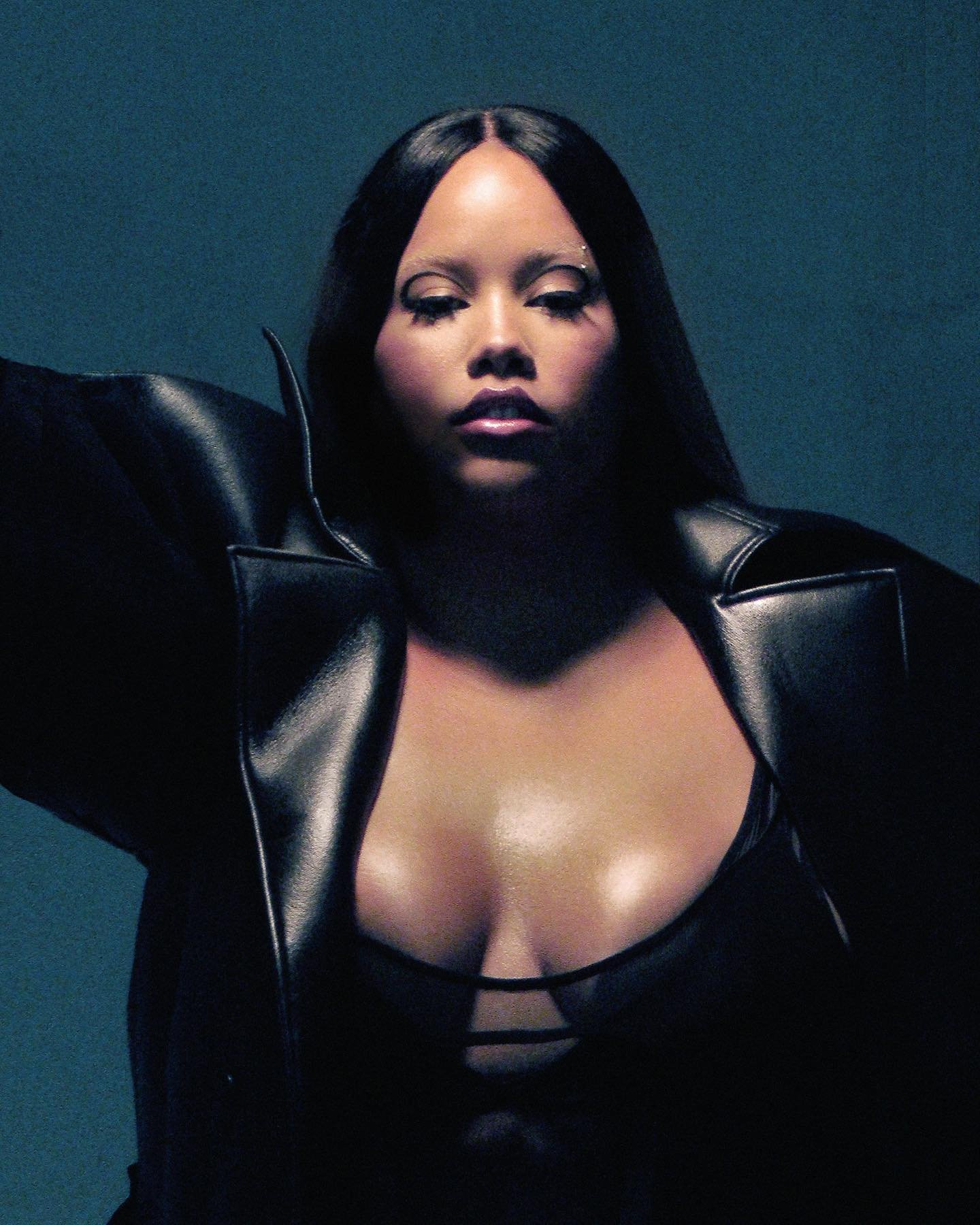 Striking portrait of a woman with dark hair wearing a black leather jacket, against a gradient grey background in a photo studio.