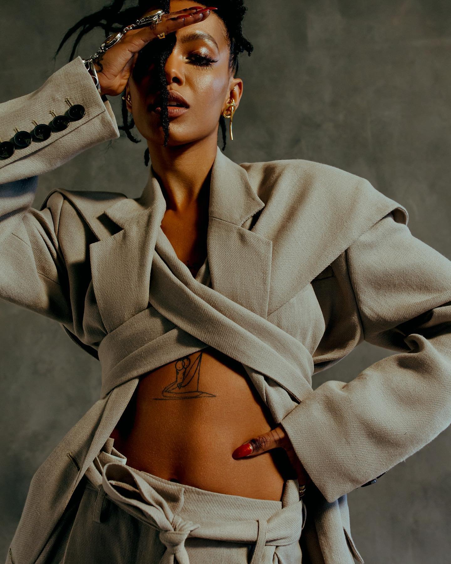 Portrait of a woman with dark hair in a light-colored blazer and matching pants. She poses with one hand over her forehead.