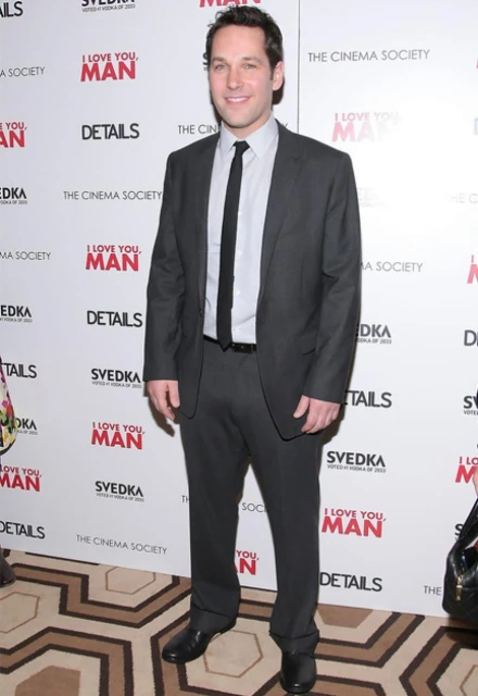 Paul Rudd posing at the premiere of 'I Love You, Man' in a dark suit and tie in front of promotional posters for the movie.