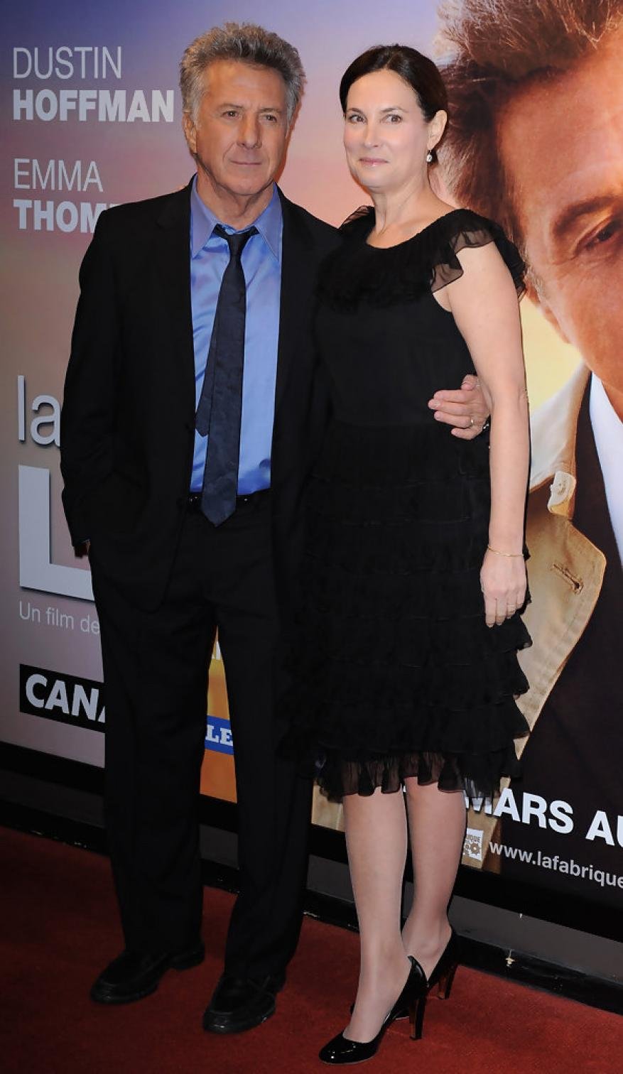 Dustin Hoffman and Lisa are posing together in front of a movie poster at a premiere. Hoffman is wearing a suit and tie.