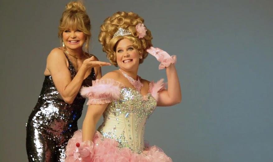 Two women pose in a photo studio, one in a sparkly dress, the other in a princess costume, against a plain grey backdrop.