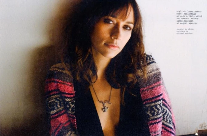 Portrait of a woman wearing a patterned cardigan and necklace against a neutral wall, styled by Leesa Evans.