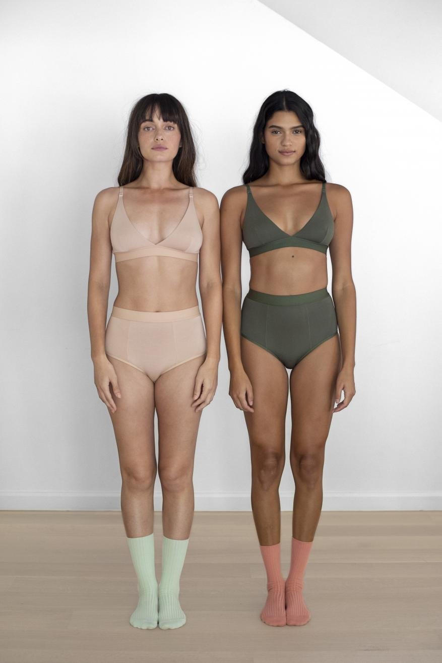Two adult women pose indoors, wearing matching bra and underwear sets in a bright, full shot on a white background.
