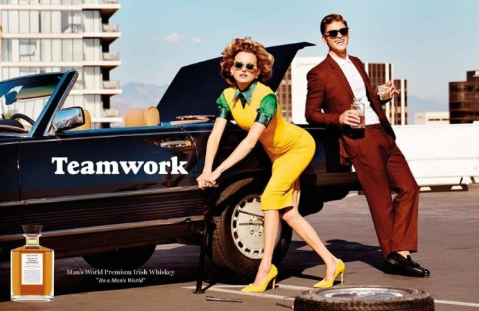 Fashion ad featuring a couple in vintage attire with a classic car, whiskey bottle, and tire in an urban outdoor setting.