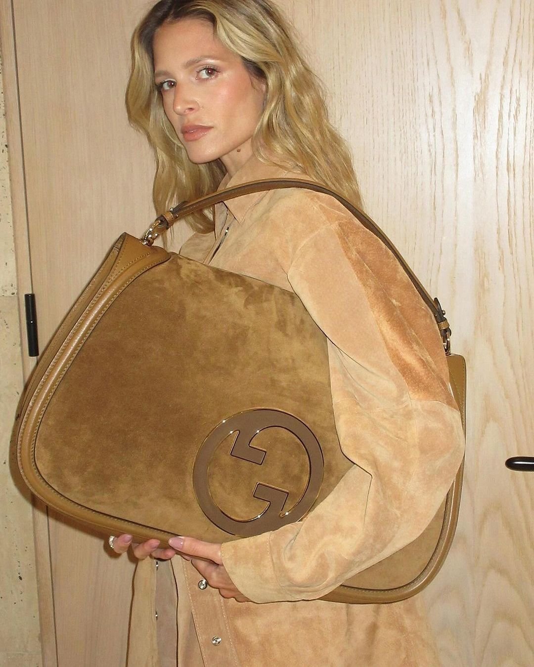 Woman poses with a Gucci handbag in a warm-toned, soft-focus studio shot, showcasing fashion and style.