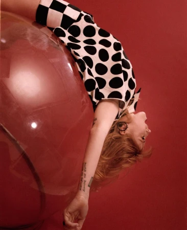 Model wearing a black and white polka dot and checkered top leaning against a large red glossy sphere.