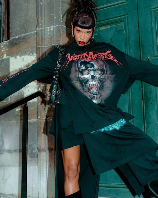 Woman in Vetements oversized skull graphic tee and black skirt poses in front of a stone building, accented by a black studded purse.