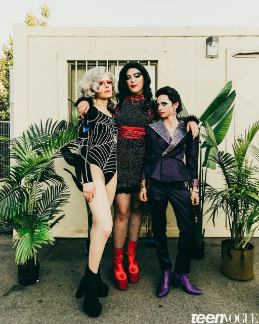 Three drag queens pose outdoors in makeup and costumes in front of a building and potted palms, fashion editorial for Teen Vogue.